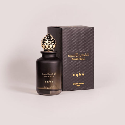 Black perfume bottle with gold cap and matching box on a light gray background