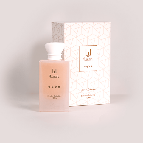 Perfume bottle with white cap and pink body next to its packaging on a light gray background